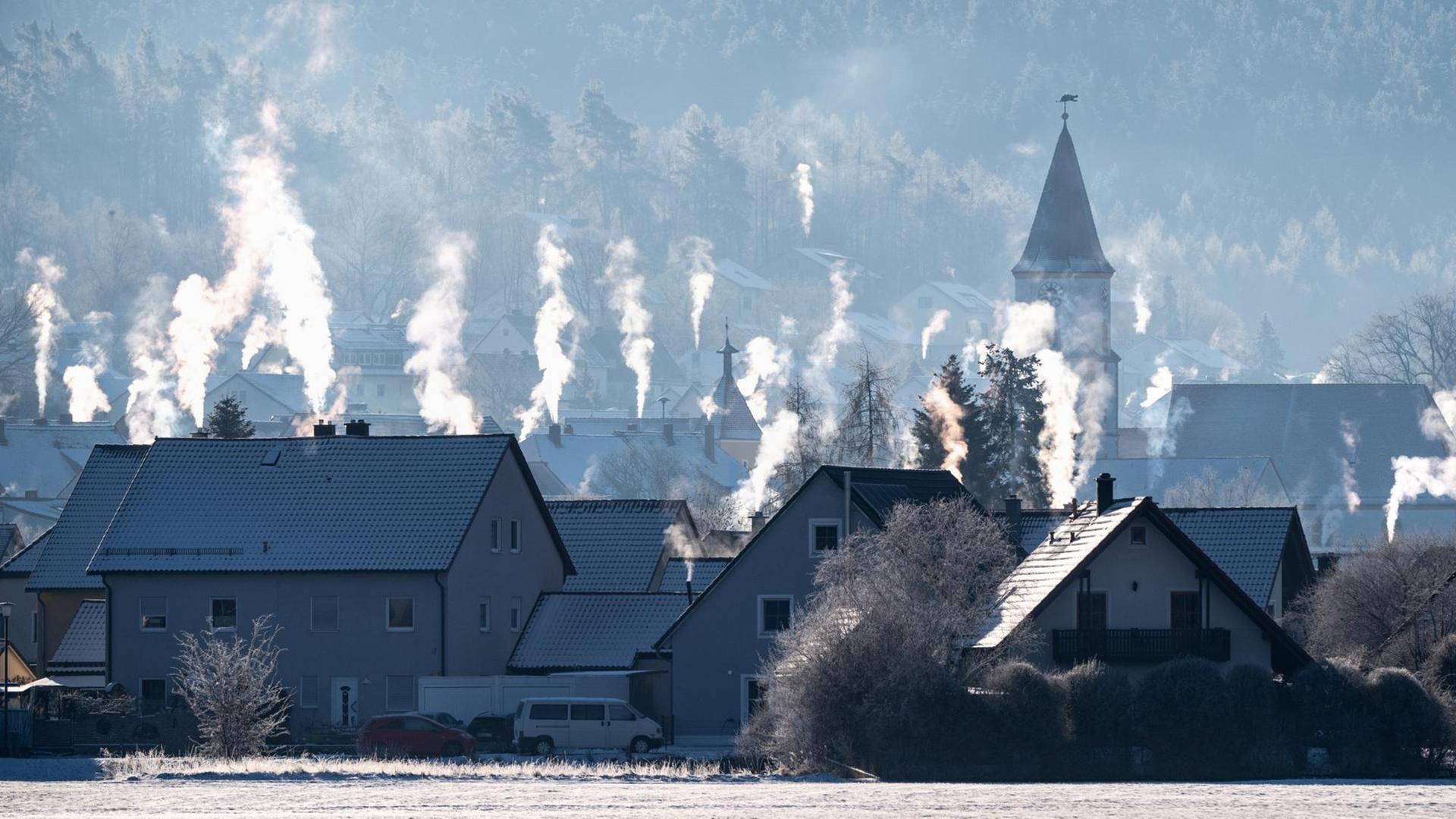 Die Schornsteine auf den Dächern der Häuser rauchen in der kalten Luft in Luthe-Wildenau.