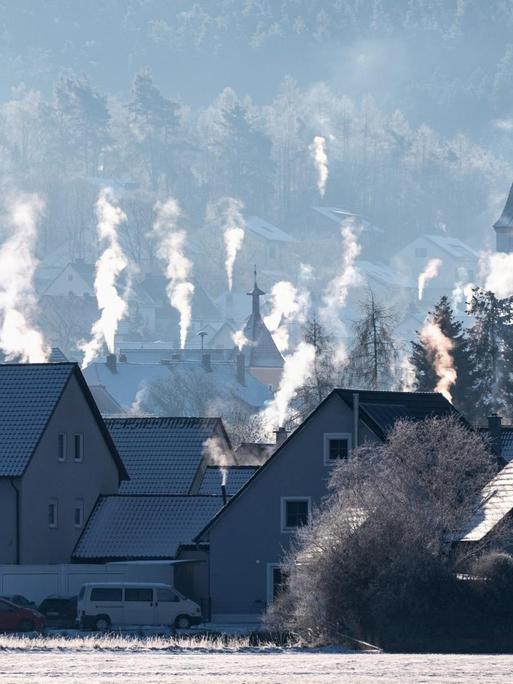 Die Schornsteine auf den Dächern der Häuser rauchen in der kalten Luft in Luthe-Wildenau.