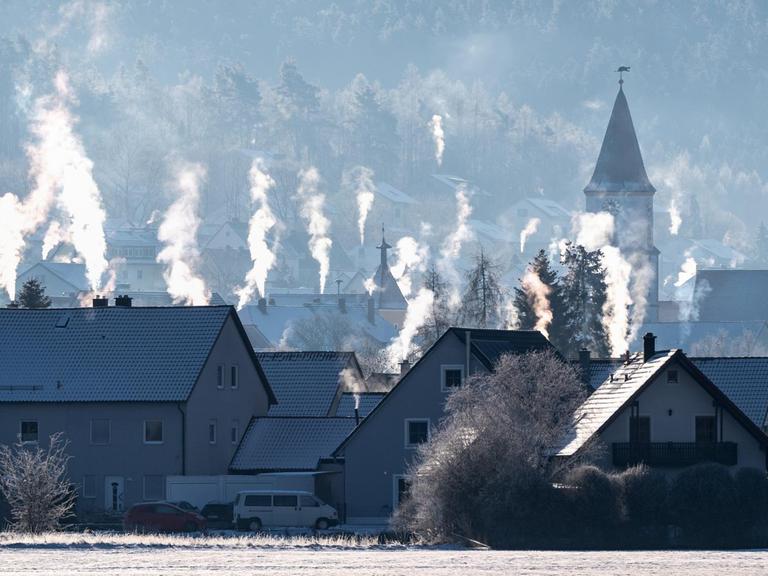 Die Schornsteine auf den Dächern der Häuser rauchen in der kalten Luft in Luthe-Wildenau.