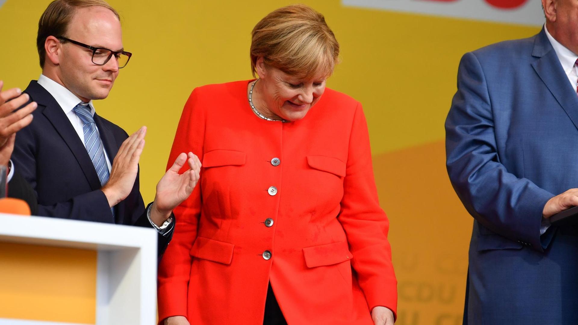 Bundeskanzlerin Angela Merkel schaut bei einer Wahlkampfveranstaltung auf einen Fleck auf ihrer Jacke. Ein Tisch, der vor ihr stand, war von einem Gegenstand aus den Reihen des Publikums getroffen worden, dabei waren Spritzer auf Merkels Jackett gekommen. Links steht der Vorsitzende der CDU Heidelberg, Alexander Föhr