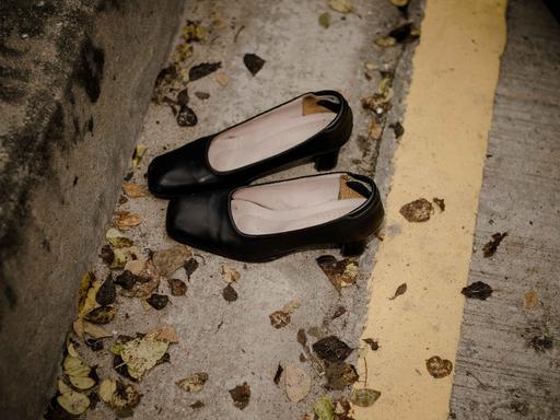 Ein Paar schwarzer ausgetretener Damenschuhe liegt auf einer Straße mit Laubblättern.
