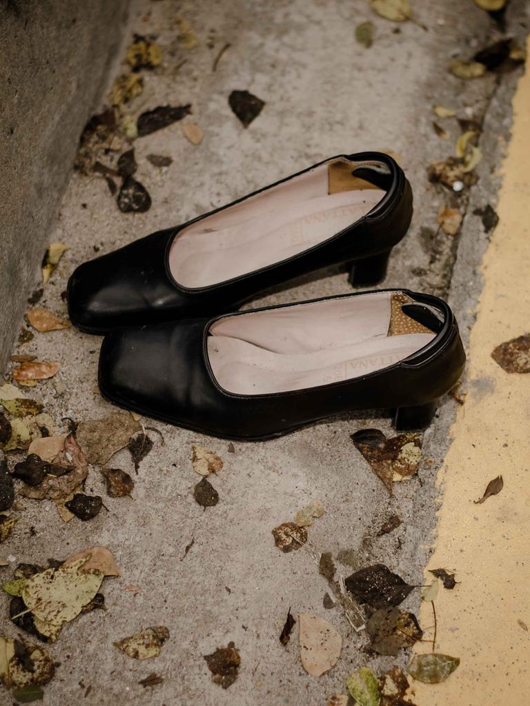 Ein Paar schwarzer ausgetretener Damenschuhe liegt auf einer Straße mit Laubblättern.