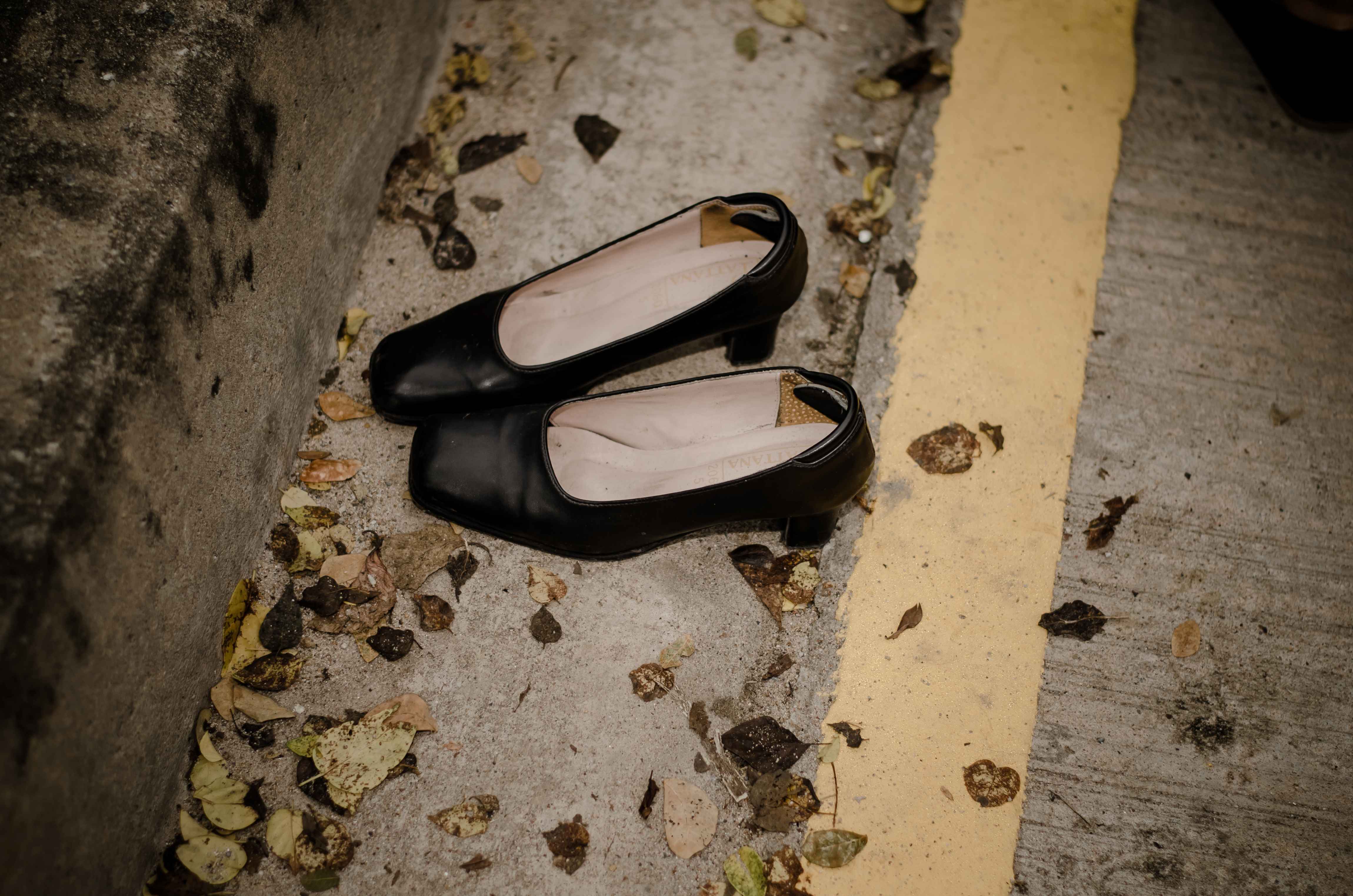 Ein Paar schwarzer ausgetretener Damenschuhe liegt auf einer Straße mit Laubblättern.
