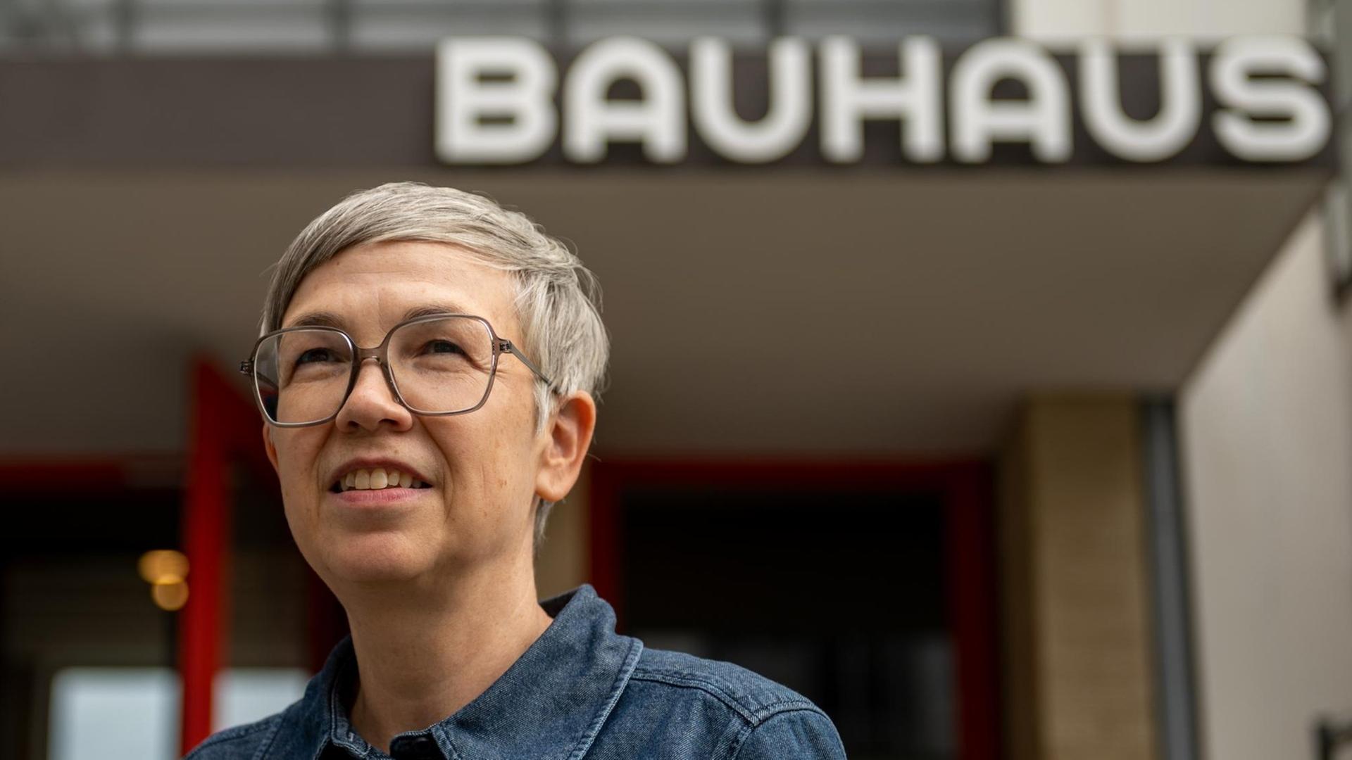Die neue Bauhaus-Direktorin Barbara Steiner, graue Harre. silberne Brille, vor einem Bauhaus-Schriftzug.
