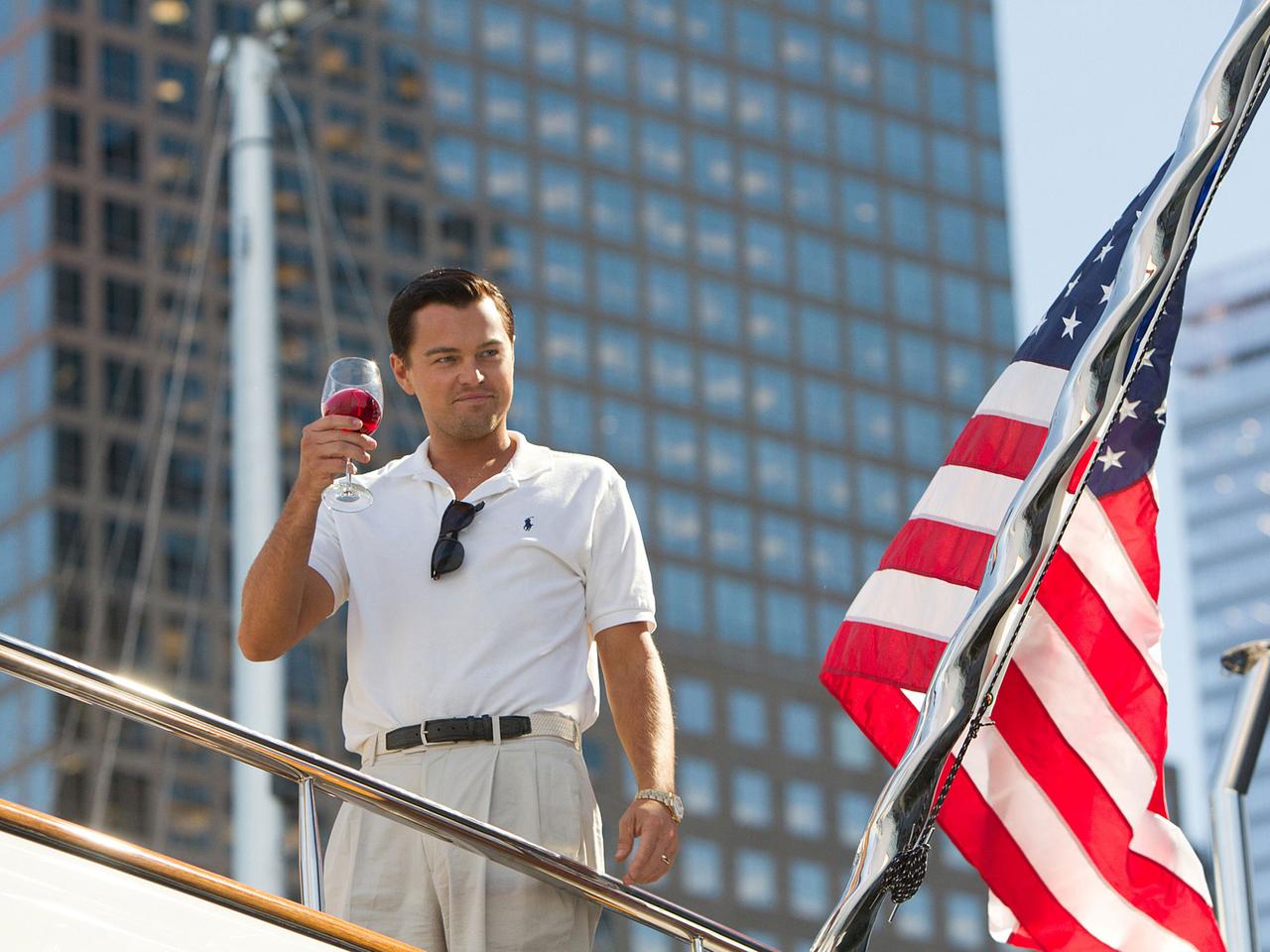 Leonardo DiCaprio steht neben einer US-Flagge auf einem Schiff und hält einen Drink hoch