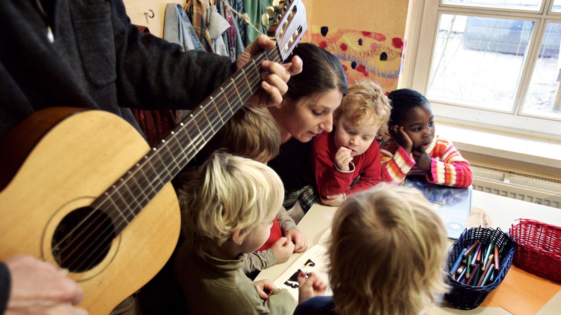 Kinder spielen in Hamburg im Kinderladen "Belle", ein Erzieher spielt Gitarre.