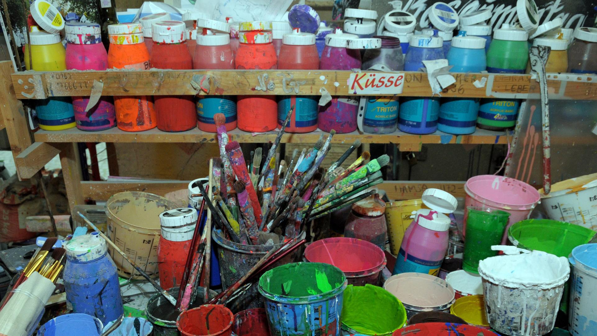 Farbtöpfe und Pinsel stehen in einem Atelier.