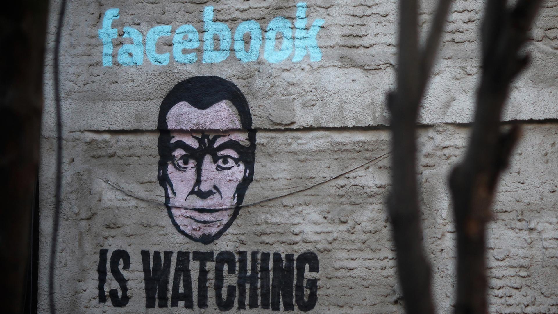 Ein Wandbild an einer Hauswand im Stadtteil Lavapiés von Madrid zeigt ein Gesicht und die Aufschrift "Facebook is watching".