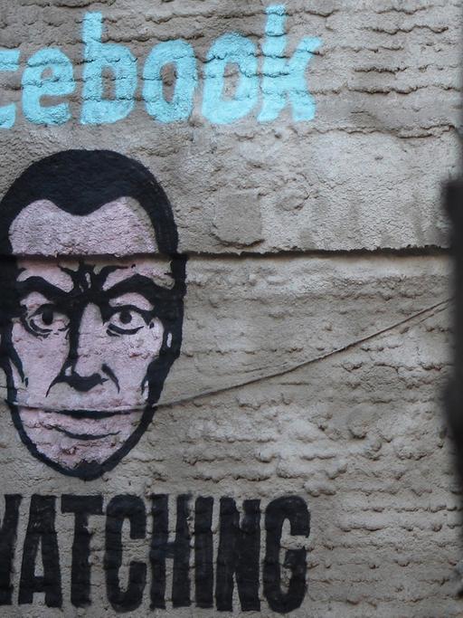 Ein Wandbild an einer Hauswand im Stadtteil Lavapiés von Madrid zeigt ein Gesicht und die Aufschrift "Facebook is watching".