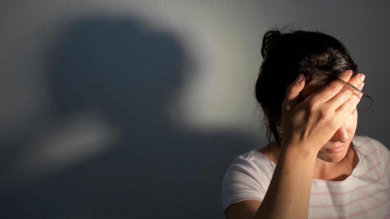 Eine Frau fasst sich an den Kopf, hinter ihr ist an der Wand ihr Schatten zu sehen. (Symbolfoto)