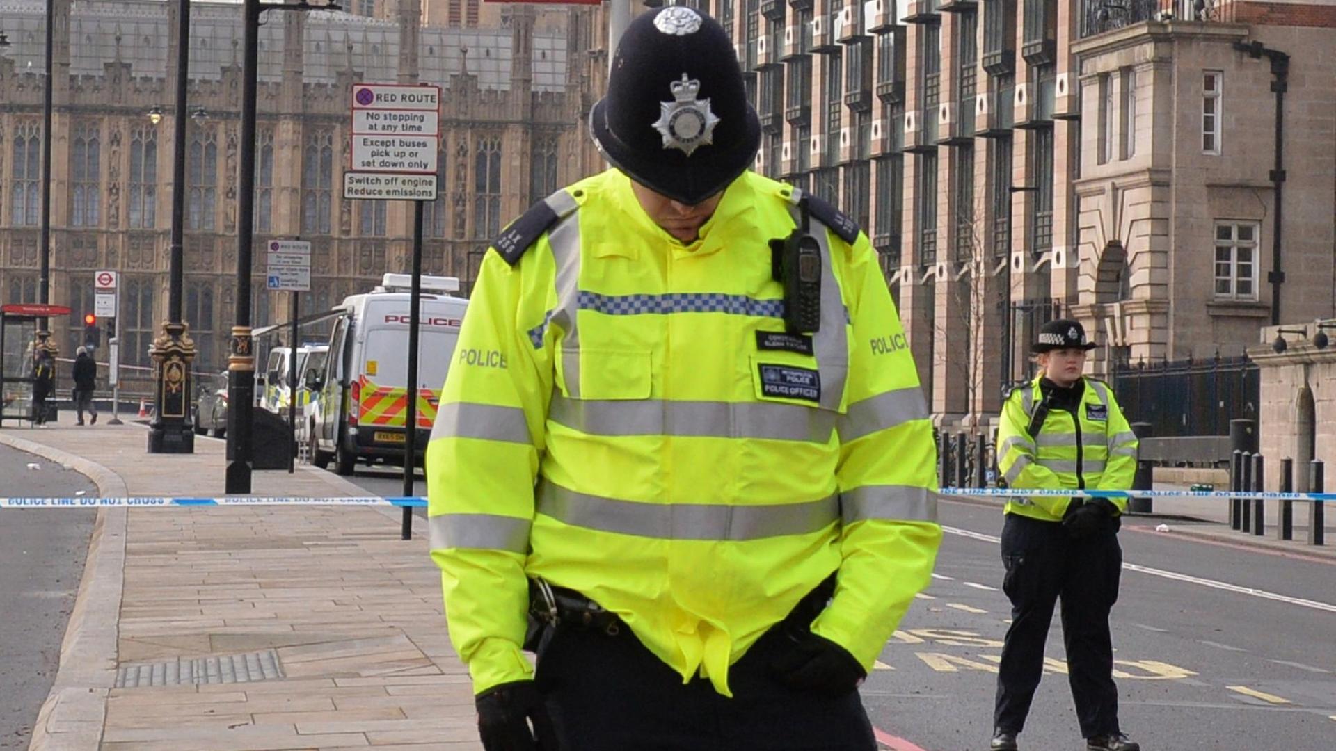 Ein Polizist in gelber Warnjacke steht auf der Straße und hat den Kopf gesenkt.