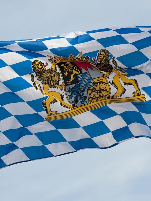 Ein blau-weiße Bayernfahne mit dem Wappen des Freistaats Bayern weht im Wind.