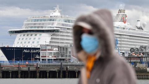 Eine Person mit Atemschutzmaske geht an dem Kreuzfahrtschiff, welches am Dock liegt, vorbei.