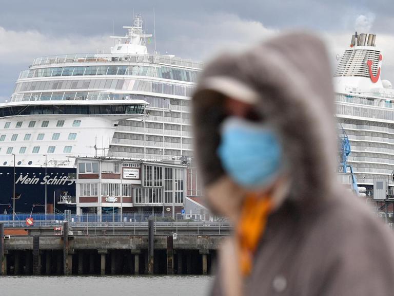 Eine Person mit Atemschutzmaske geht an dem Kreuzfahrtschiff, welches am Dock liegt, vorbei.