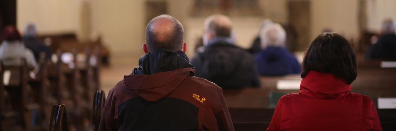 Besucher sitzen aufgrund der Corona-Pandemie mit Abstand zueinander in einer Kirche