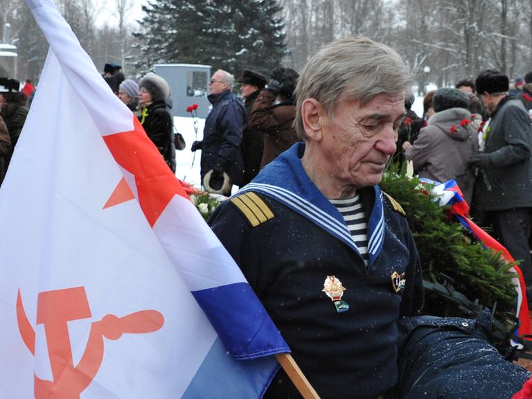 Ein Mann trägt bei einer Gedenkfeier in St. Petersburg die sowjetische Marineflagge.