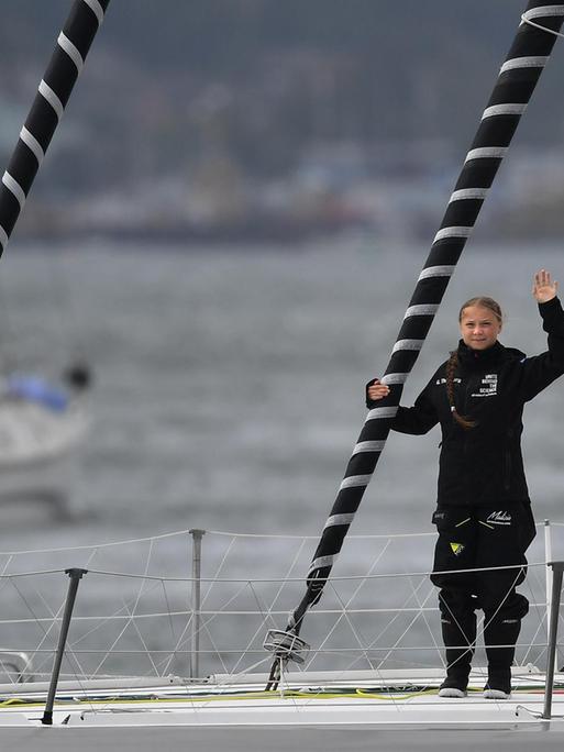 Greta Thunberg steht auf dem Deck des Segelbootes und winkt Richtung Kamera.