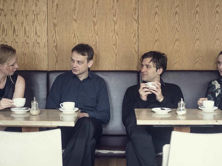 Die vier Musiker sitzen nebeneinander in einem Kaffe und sind in ein Gespräch vertieft