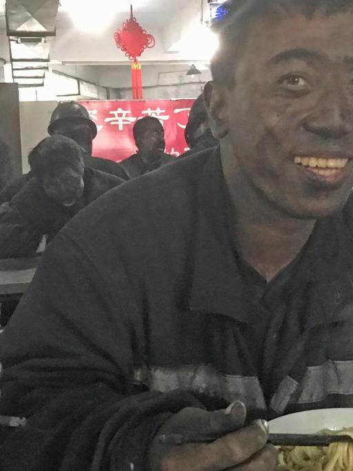An einem Imbissstand im Kohlerevier von Yangquan sitzt ein Arbeiter mit schwarzem Kopf und isst Nudelsuppe.