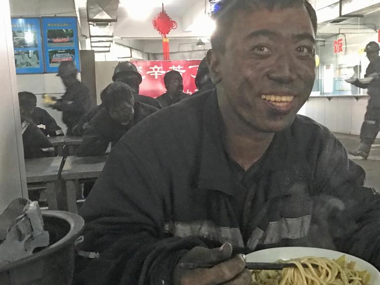 An einem Imbissstand im Kohlerevier von Yangquan sitzt ein Arbeiter mit schwarzem Kopf und isst Nudelsuppe.