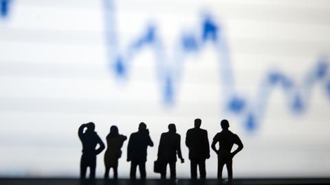 Miniaturfiguren stehen vor einer Börsenkurve