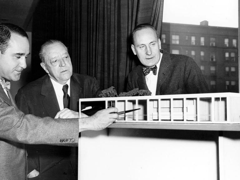 Der Architekt Ludwig Mies van der Rohe (M) mit Herbert S. Greenwald (l) und Robert H. McCormick jr. (r) vor dem Modell eines von ihm entworfenen und in Chicago gebauten Hauses aus Glas und Stahl (undatiert).