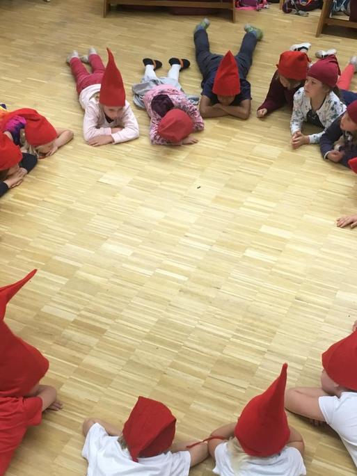 In einer Kölner Waldorfschule liegen die Kinder im Kreis - sie tragen rote Zipfelmützen