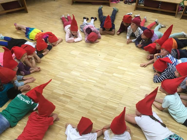 In einer Kölner Waldorfschule liegen die Kinder im Kreis - sie tragen rote Zipfelmützen