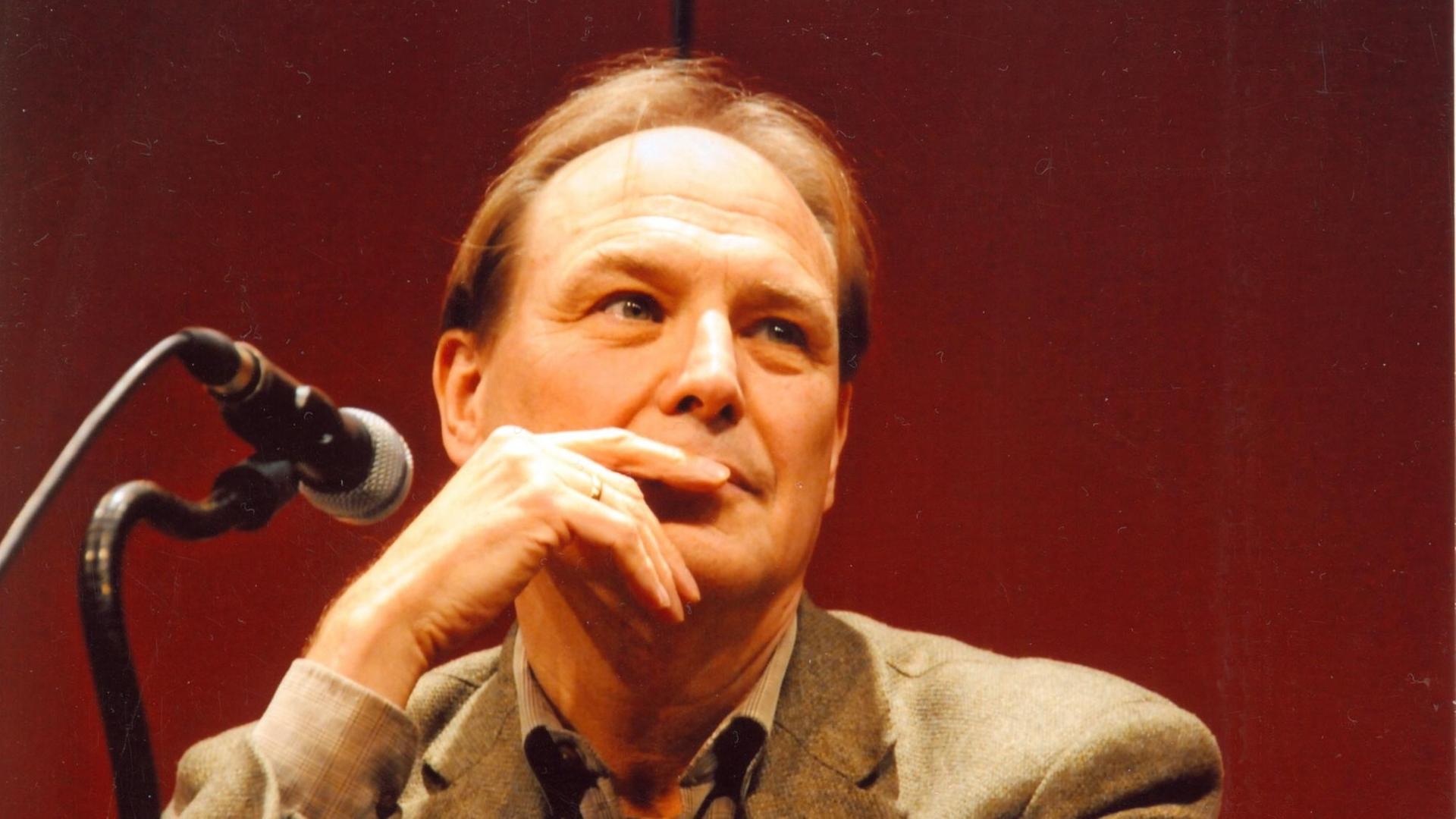 Michael Walter sitzt an einem Tisch mit Mikrofon, vor einem roten Hintergrund