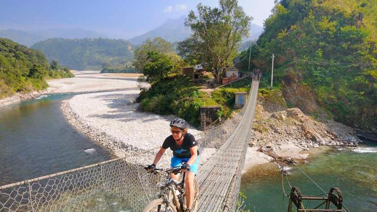 Eine Dame fährt auf einem Mountainbike über eine hängende Brücke.