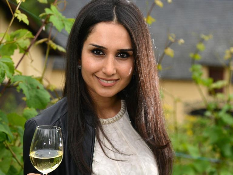 Ninorta Bahno aus Syrien posiert am 28.06.2016 in einem Weinberg in Trier (Rheinland-Pfalz) mit einem Glas Riesling-Wein.