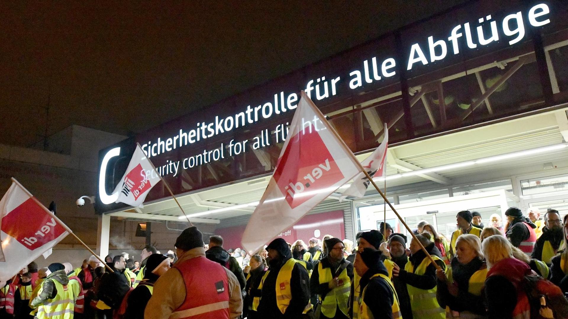 Auf dem Foto zu sehen sind Streikende mit Ver.di-Flaggen vor dem Flughafengebäude.