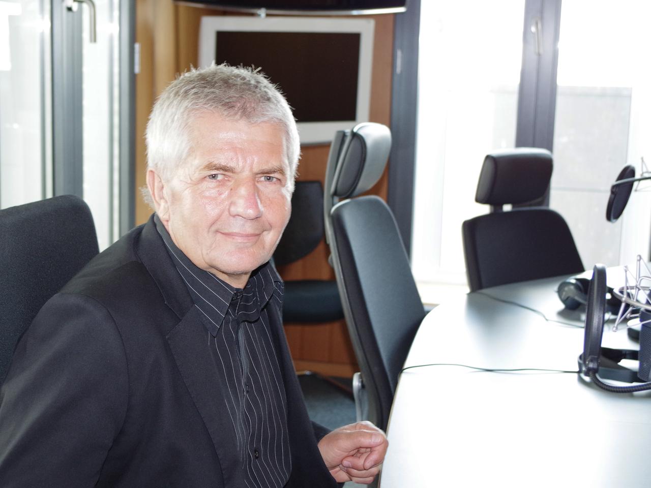 Roland Jahn sitzt an einem Tisch vor einem Mikrofon in einem Studio des Hauptstadtbüro des Deutschlandfunks und lächelt in die Kamera.