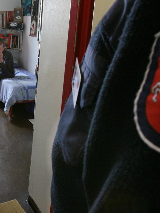 Ein 19-jähriger Häftling sitzt in seiner Zelle im Jugendgefängnis Hameln, im Vordergrund ist das niedersächsische Justizabzeichen auf dem Ärmel eines Justizbeamten zu sehen.