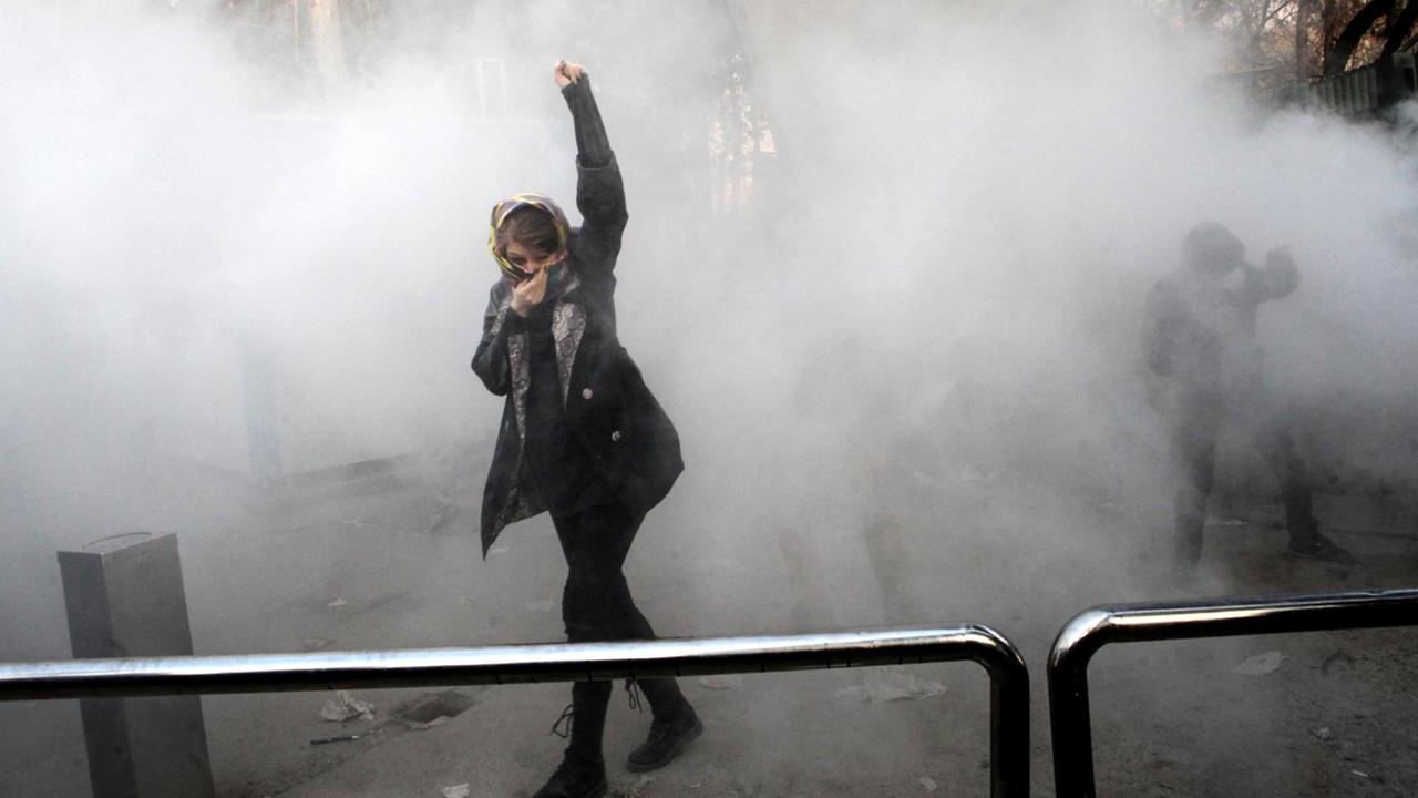 An Iranian woman raises her fist amid the smoke of tear gas at the University of Tehran during a protest driven by anger over economic problems, in the capital Tehran on December 30, 2017. Students protested in a third day of demonstrations sparked by anger over Iran's economic problems, videos on social media showed, but were outnumbered by counter-demonstrators. / AFP PHOTO / STR
