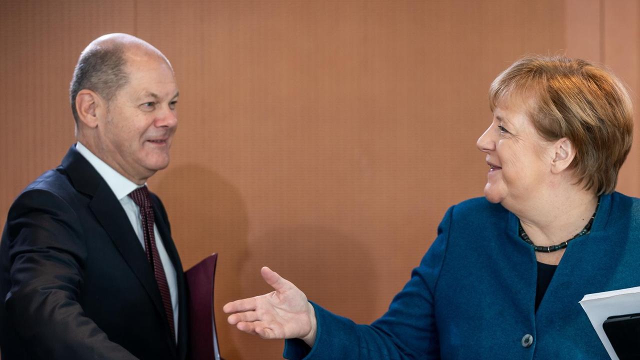 Bundeskanzlerin Merkel und Finanzminister Scholz sitzen nebeneinander am Kabinettstisch und lächeln.