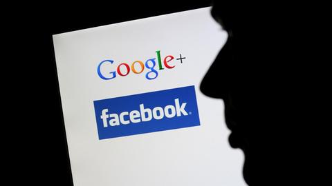 Die Silhouette eines Mannes zeichnet sich vor einem Computerbildschirm mit den Logos von Google+ und Facebook ab.