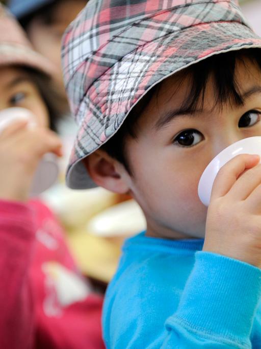 Japanische Kinder mit Hut, die aus Bechern trinken