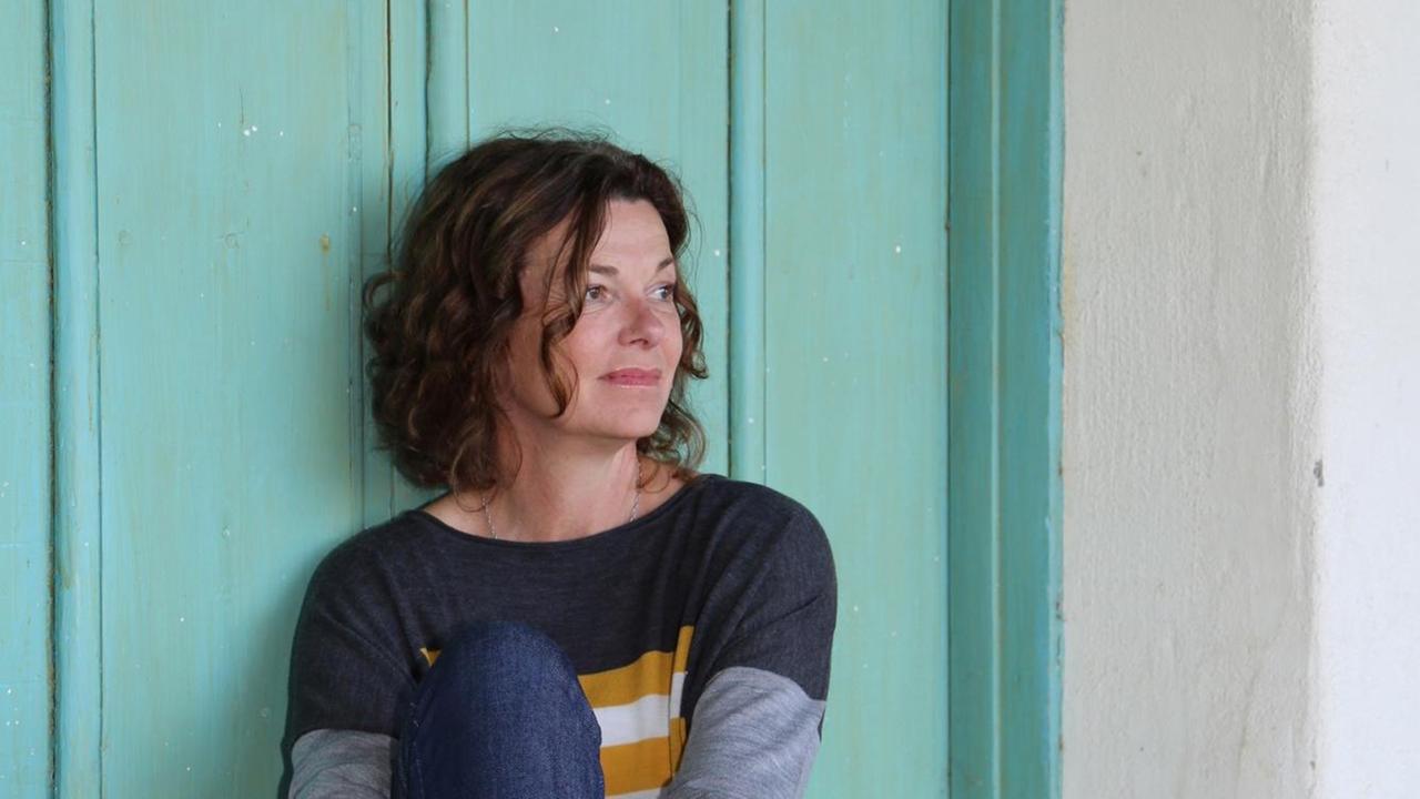 Die Schweizer Schriftstellerin Milena Moser vor einer tuerkisen Wand sitzend.