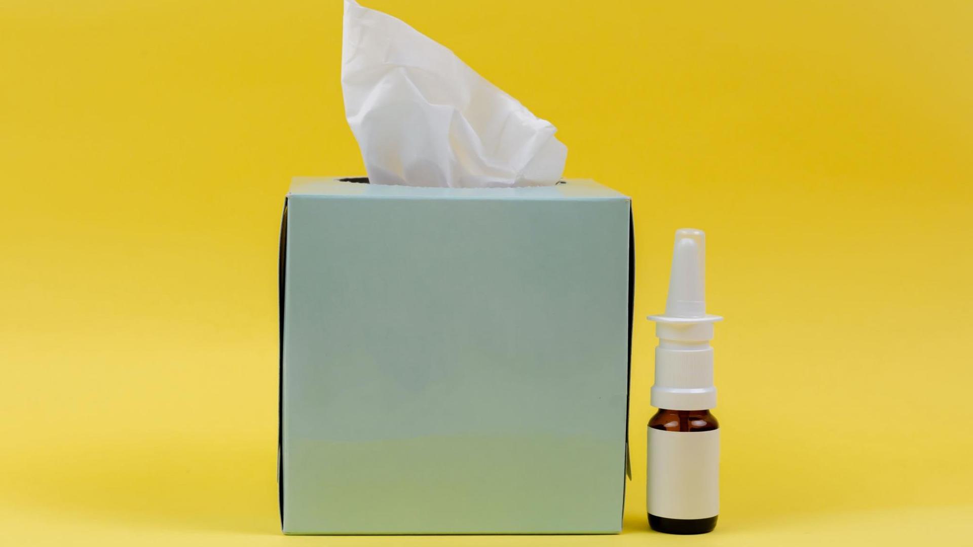 Eine Taschentuchbox und ein Fläschen Nasenspray vor gelbem Hintergrund
