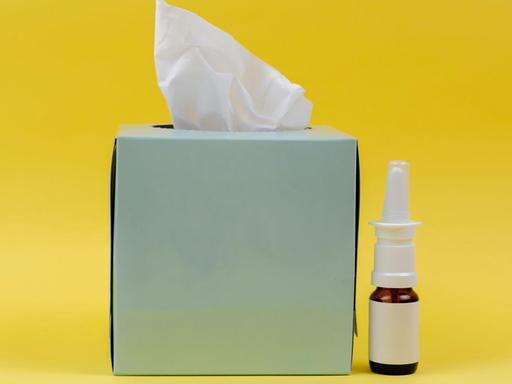 Eine Taschentuchbox und ein Fläschen Nasenspray vor gelbem Hintergrund