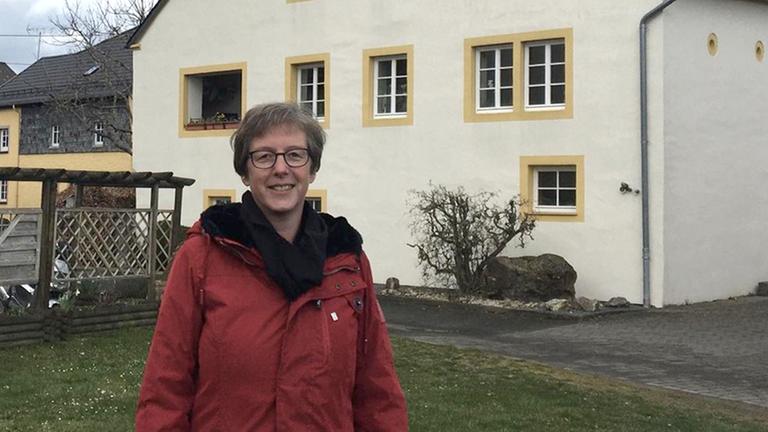 Petra Fischer, Ortsbürgermeisterin in Oberkail, Eifelkreis Bitburg-Prüm, steht vor einem Haus.