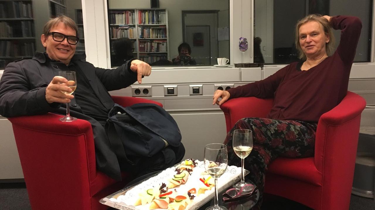Sven Regener und Elke Heidenreich sitzen in einem Deutschlandfunkbüro aus Sesseln mit einem Glas Wein in der Hand