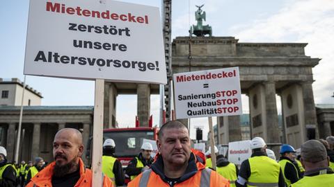 09.12.2019, Berlin: Demonstranten stehen bei einer Kundgebung eines Bündnisses der Berliner Bau- und Wohnungswirtschaft und von Vermietern gegen den Mietendeckel vor dem Brandenburger Tor mit einem Schild mit der Aufschrift "Mietendeckel zerstört unsere Altersvorsorge". Mit dem Mietendeckel will das Land Berlin die Mieten einfrieren und eine Mietobergrenze festlegen. Foto: Fabian Sommer/dpa | Verwendung weltweit