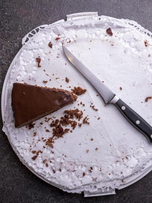 Ein letztes Kuchenstück liegt neben einem Messer auf der Kuchenplatte.