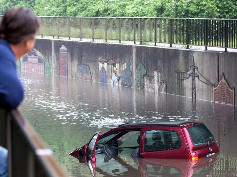 Ein Mann schaut sich am 30.05.2016 in Oberhausen (Nordrhein-Westfalen) ein Auto in einer überfluteten Straßenunterführung an.