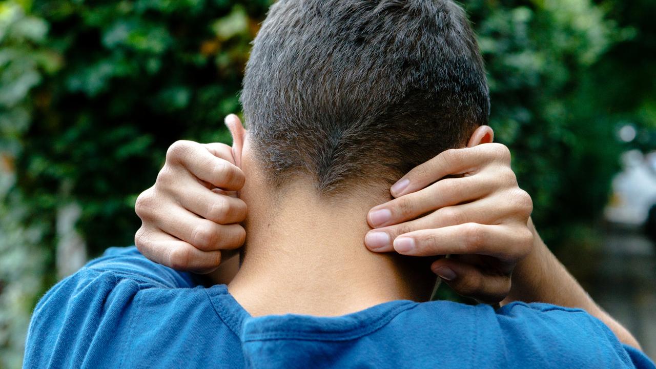 Das Bild zeigt einen von hinten fotografierten, autistischen jungen Mann. Er hält sich die Ohren zu.