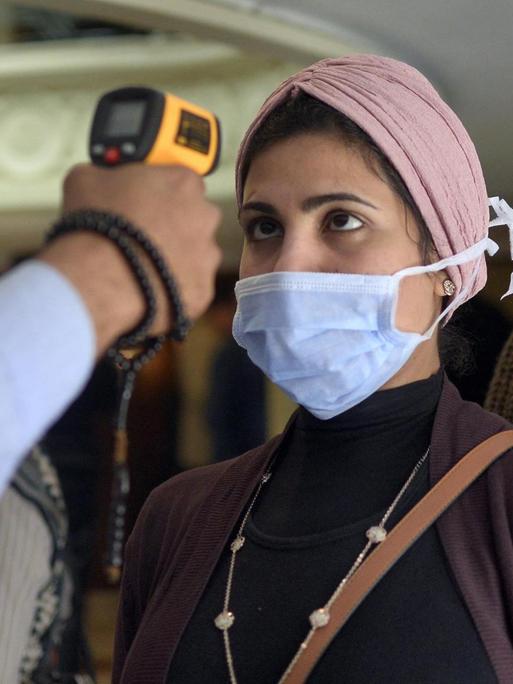 Einer Frau mit Maske wird auf einem Boot in der ägyptischen Stadt Luxor die Körpertemperatur gemessen.