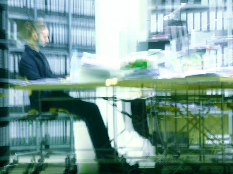 Ein Mann sitzt abends in einem Büro an einem vollen Schreibtisch und arbeitet in Berlin.