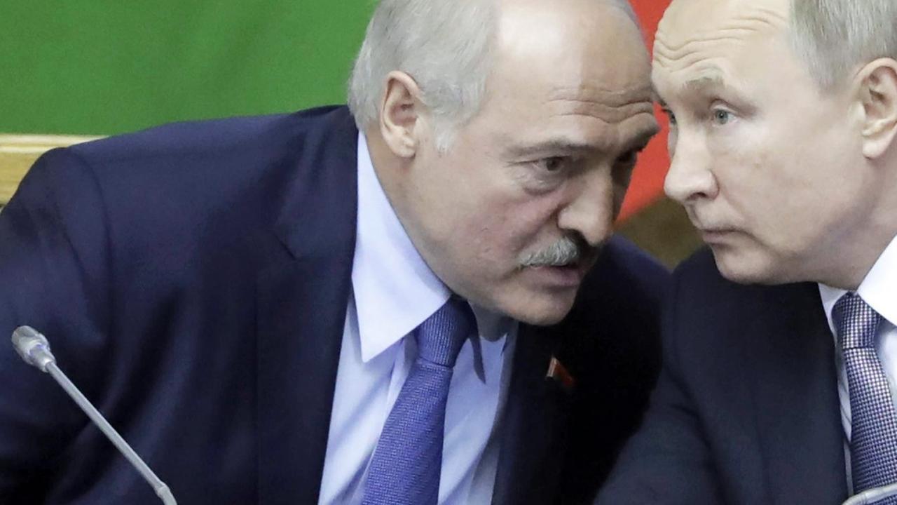 Wladimir Putin sprechen und Alexander Lukaschenko sprechen auf einem Podium leise miteinander.